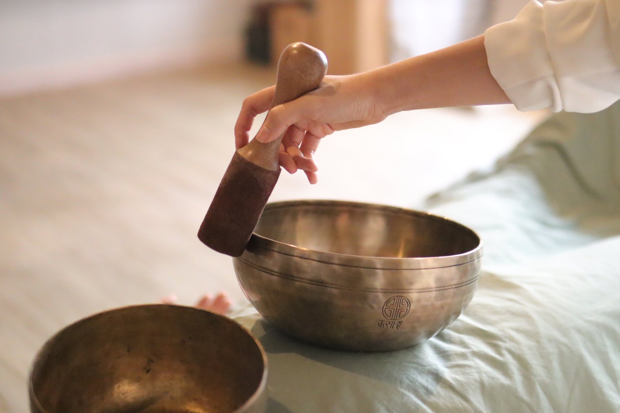 A hand playing a Tibetan singing bowl with a felt mallet