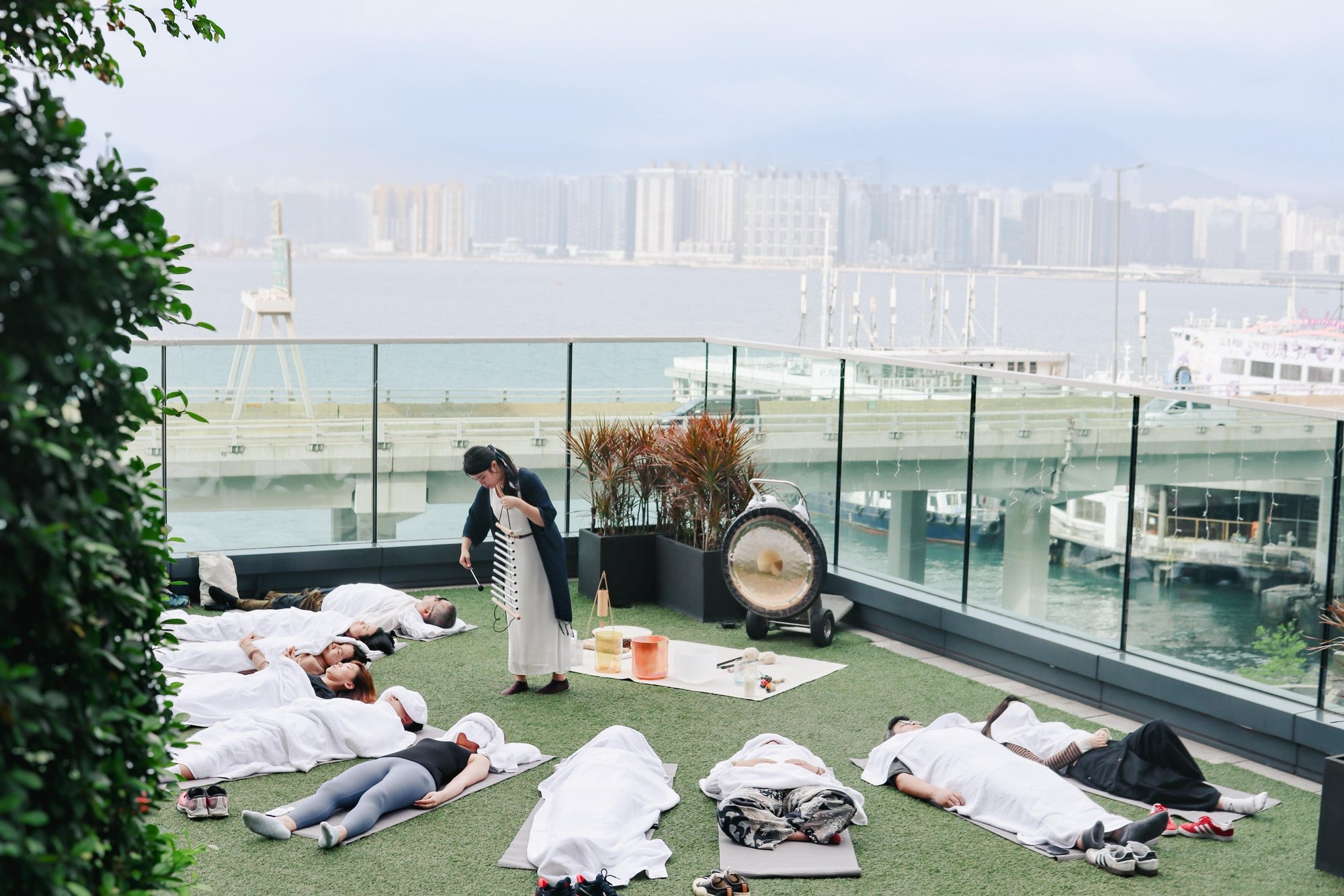 Helen playing chimes for guests resting on a harbour-view rooftop