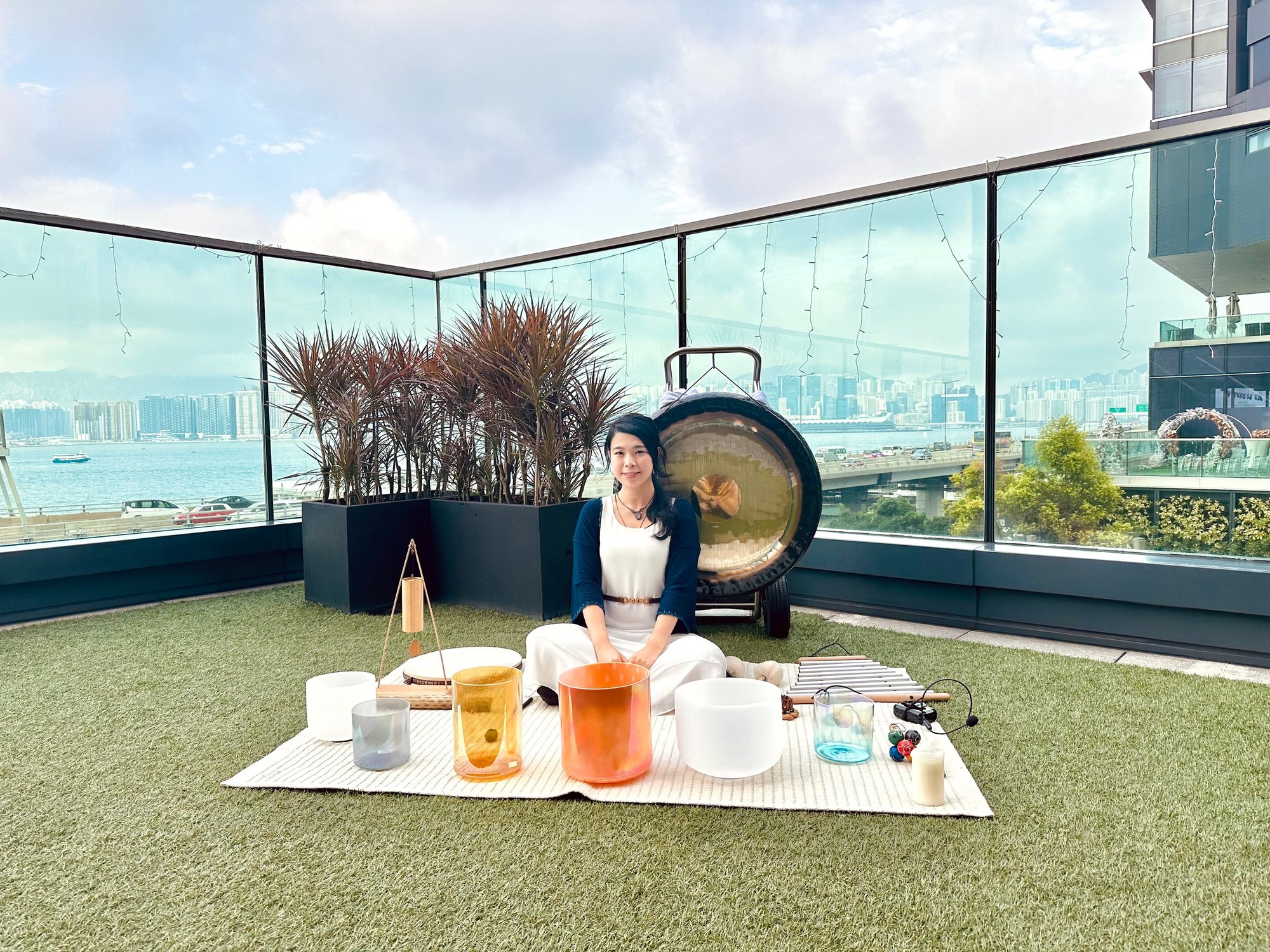 Helen seated with crystal bowls and a gong on a harbour-view rooftop