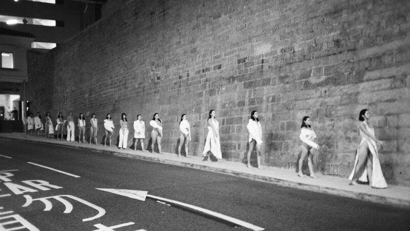 Performers in white along a stone wall