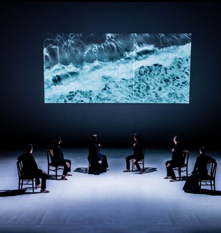 Performers seated beneath projected waves